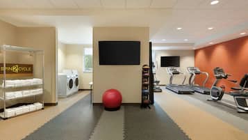 A gym with a treadmill, elliptical, stationary bike, and a red exercise ball. There is a wall-mounted TV and a laundry area with a washing machine and dryer.