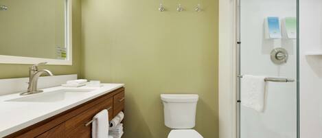 A bathroom with a white sink, vanity, and toilet. There are three towel hooks on the wall.