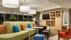 Un espace de détente moderne avec un canapé vert, une table ronde, un fauteuil rouge et un téléviseur posé sur un meuble en bois.