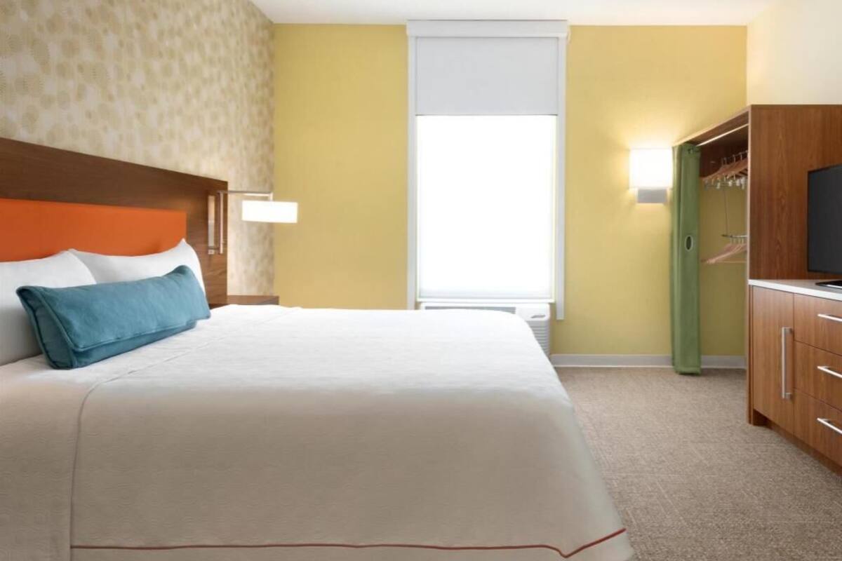 Une chambre d’hôtel équipée d’un lit, d’une armoire, d’une télévision et d’une fenêtre avec des stores.