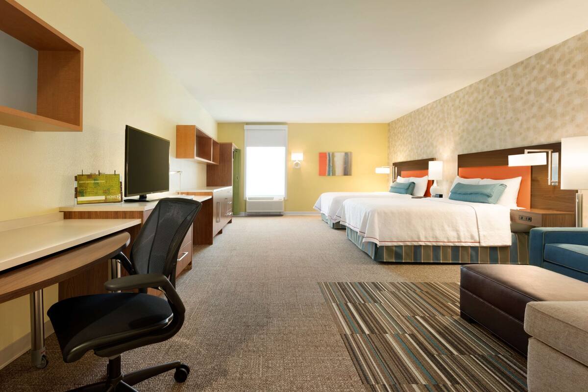 Une chambre d’hôtel équipée d’un bureau, d’une chaise, de deux lits et d’un téléviseur.