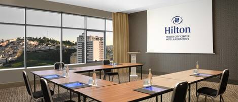 A conference room with a large screen displaying the Hilton logo, a city view, and a carpeted floor.