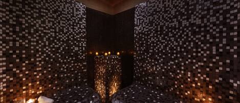 A room with mosaic-tiled walls and two seating areas with candles.