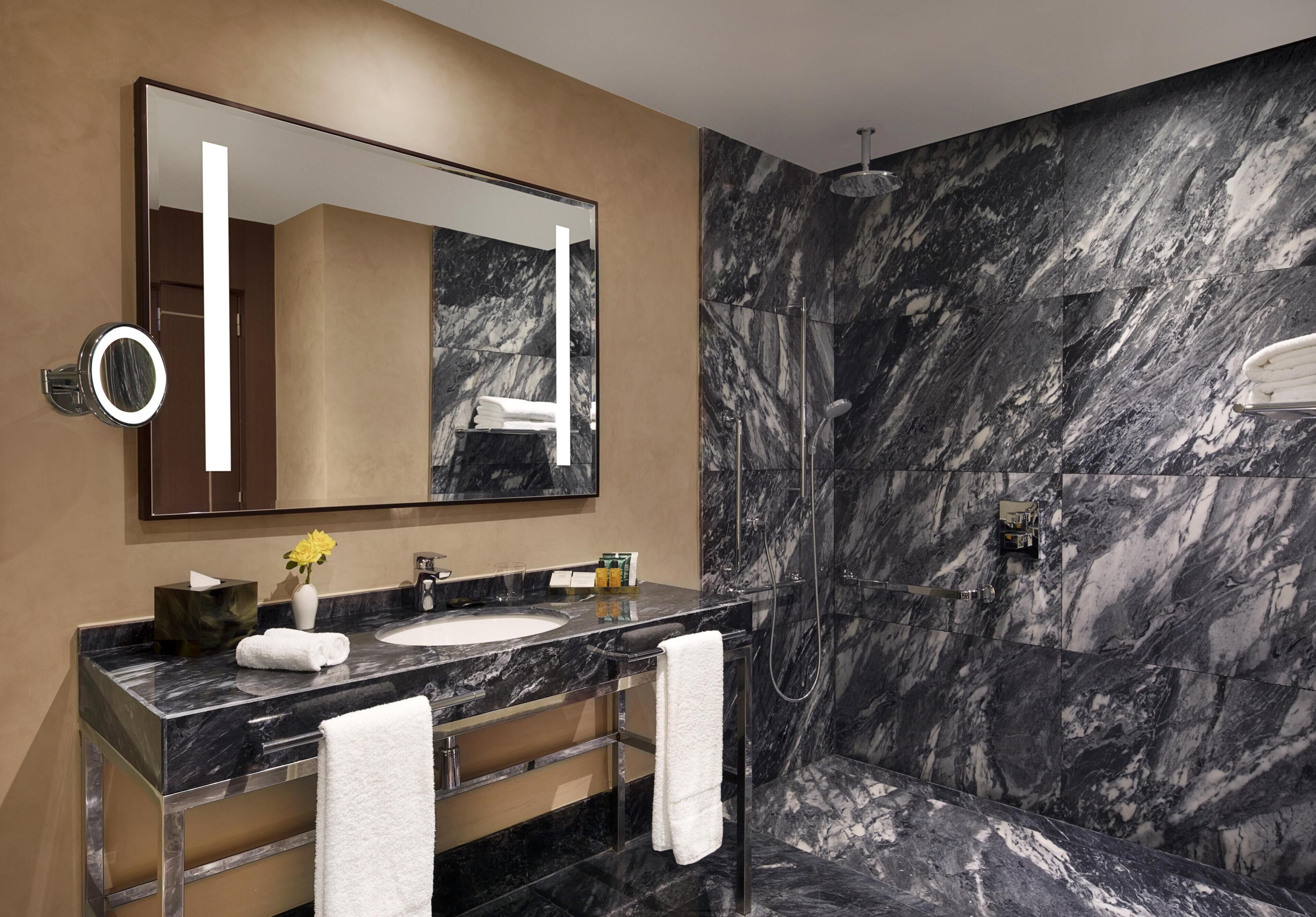 A modern bathroom with a marble shower wall, a large mirror, and a vanity with a sink and towel rack.