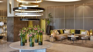 A modern lobby with a circular marble table, a multi-tiered light fixture, and a sectional sofa with ottomans.