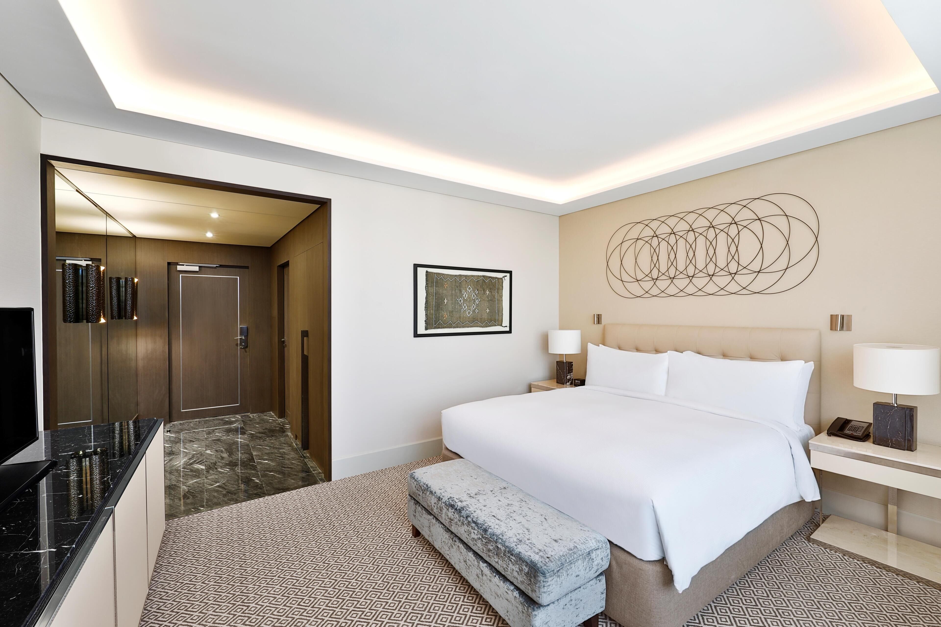 Une chambre d’hôtel comprenant un lit, des tables de chevet, un bureau, un miroir et une moquette à motifs.