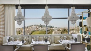 A modern dining area with a city view, a sofa, dining table, chairs, and decorative hanging lights.