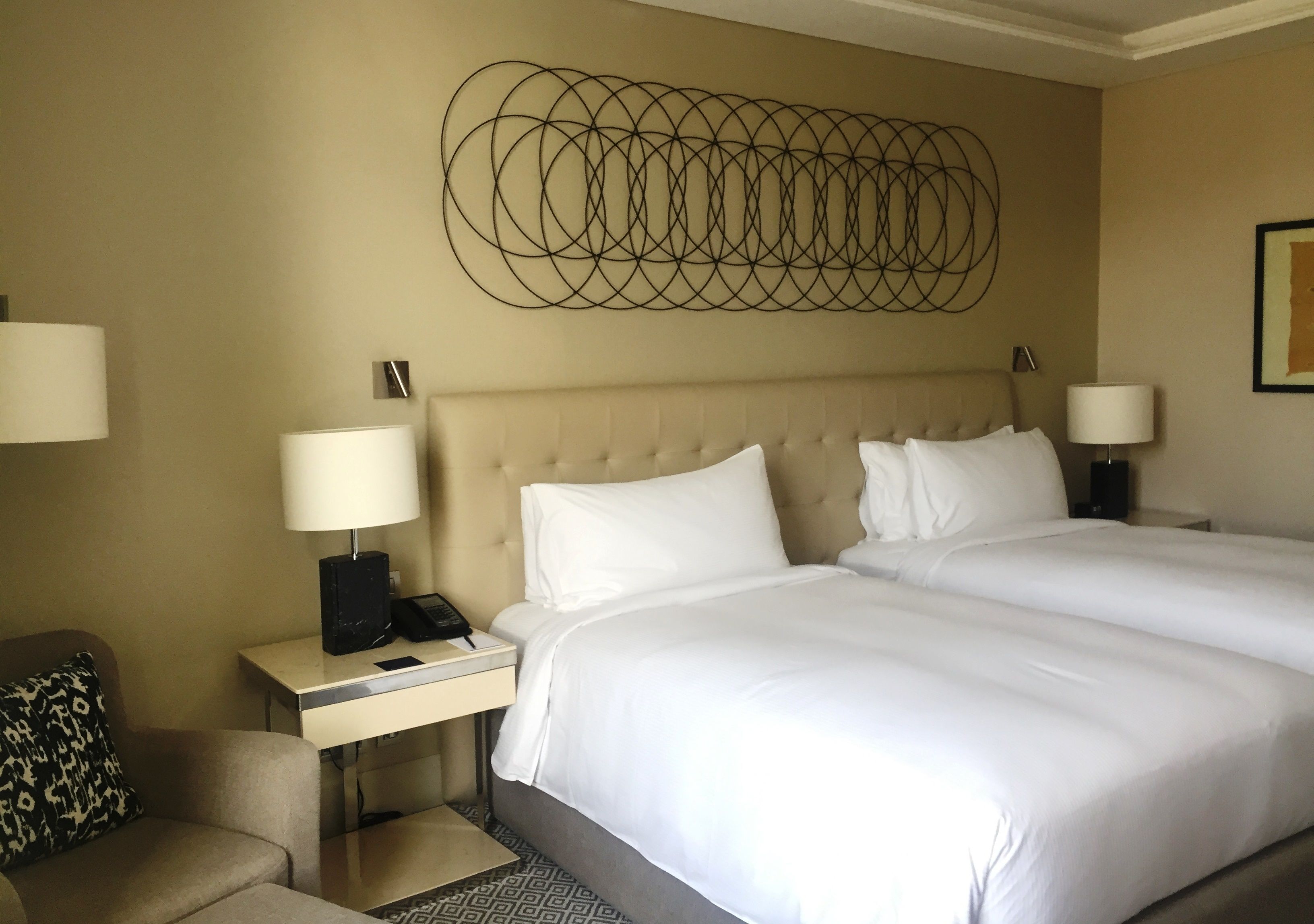 A hotel room with a large bed, two bedside tables with lamps, a patterned throw on the bed, and a wall art piece above the bed.
