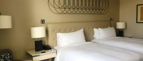 Habitación de hotel con una cama grande, dos mesitas de noche con lámparas, un plaid estampado sobre la cama y una obra de arte en la pared sobre la cama.