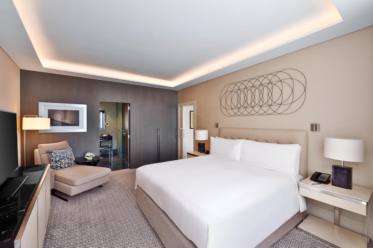 A modern hotel room with a large bed, a desk, a chair, a TV, and a wall art piece.