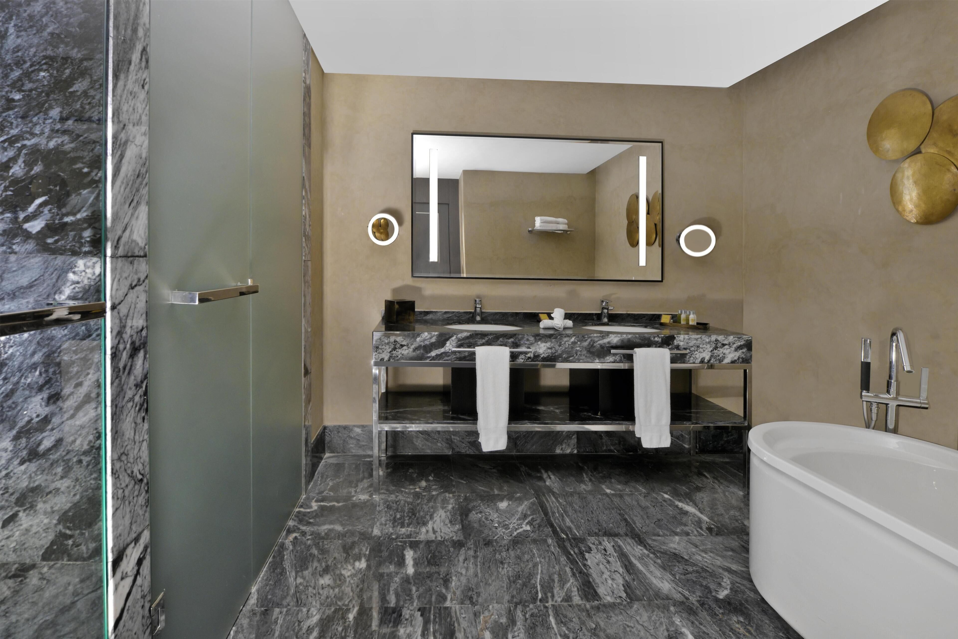 Une salle de bain moderne avec une douche à l’italienne en verre, un lavabo en marbre et une baignoire sur pieds.