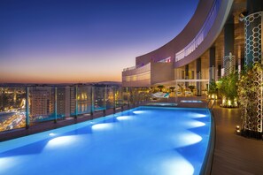 A rooftop infinity pool with a city view, a curved building with large windows, and a wooden deck with lounge chairs. - Hilton Tangier City Center (Tangier)