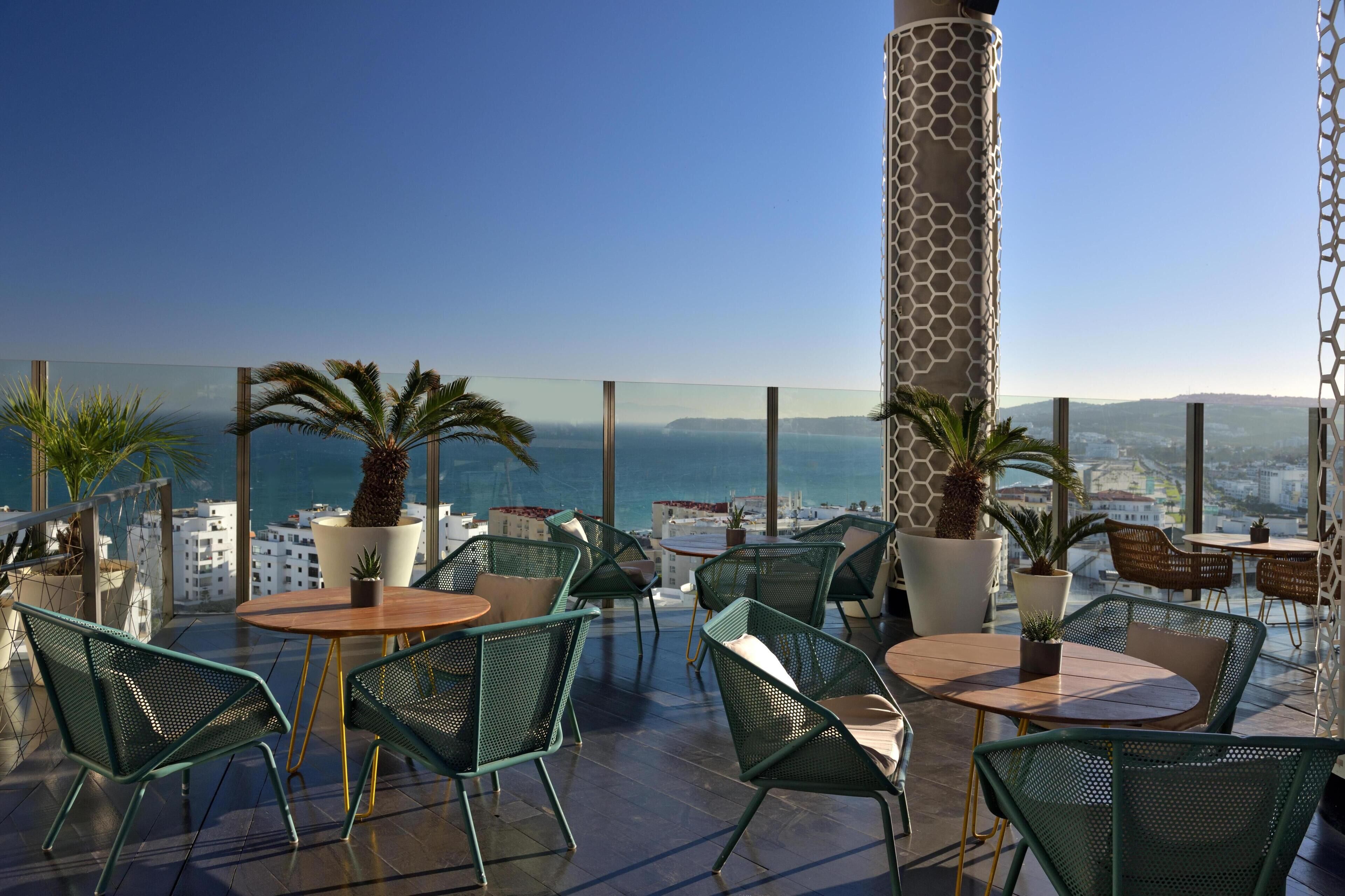 A rooftop terrace with outdoor seating, potted plants, and a view of the city and sea.