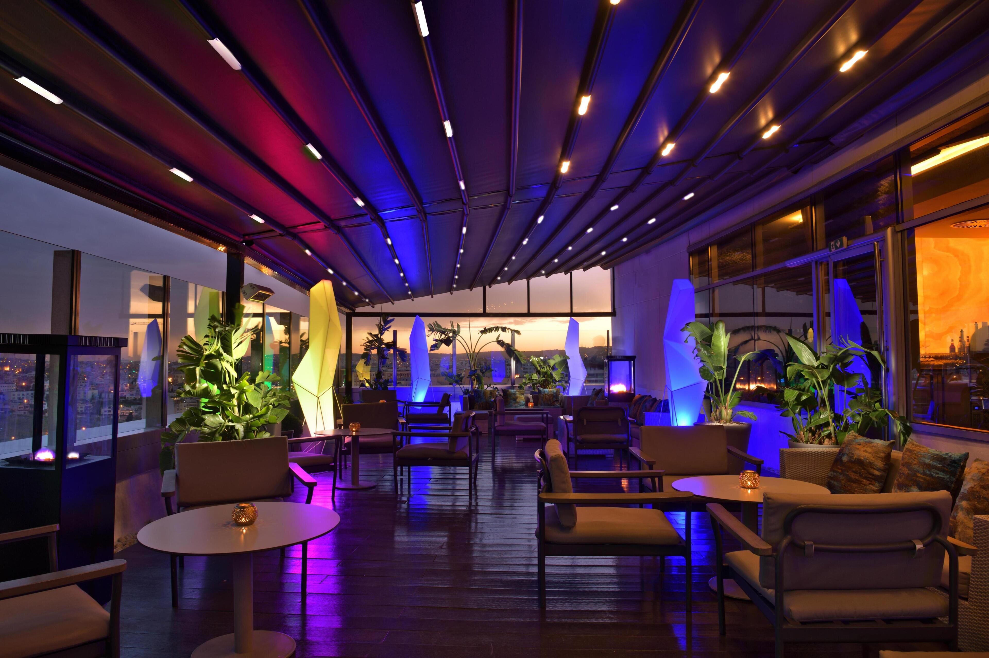 A modern lounge area with seating, potted plants, and large windows.