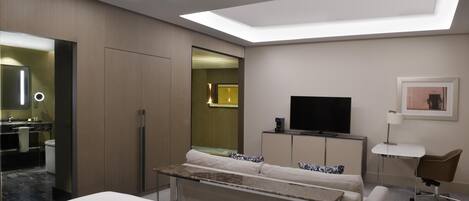 A modern hotel room with a bed, a TV, a desk, and a bathroom visible through an open door.