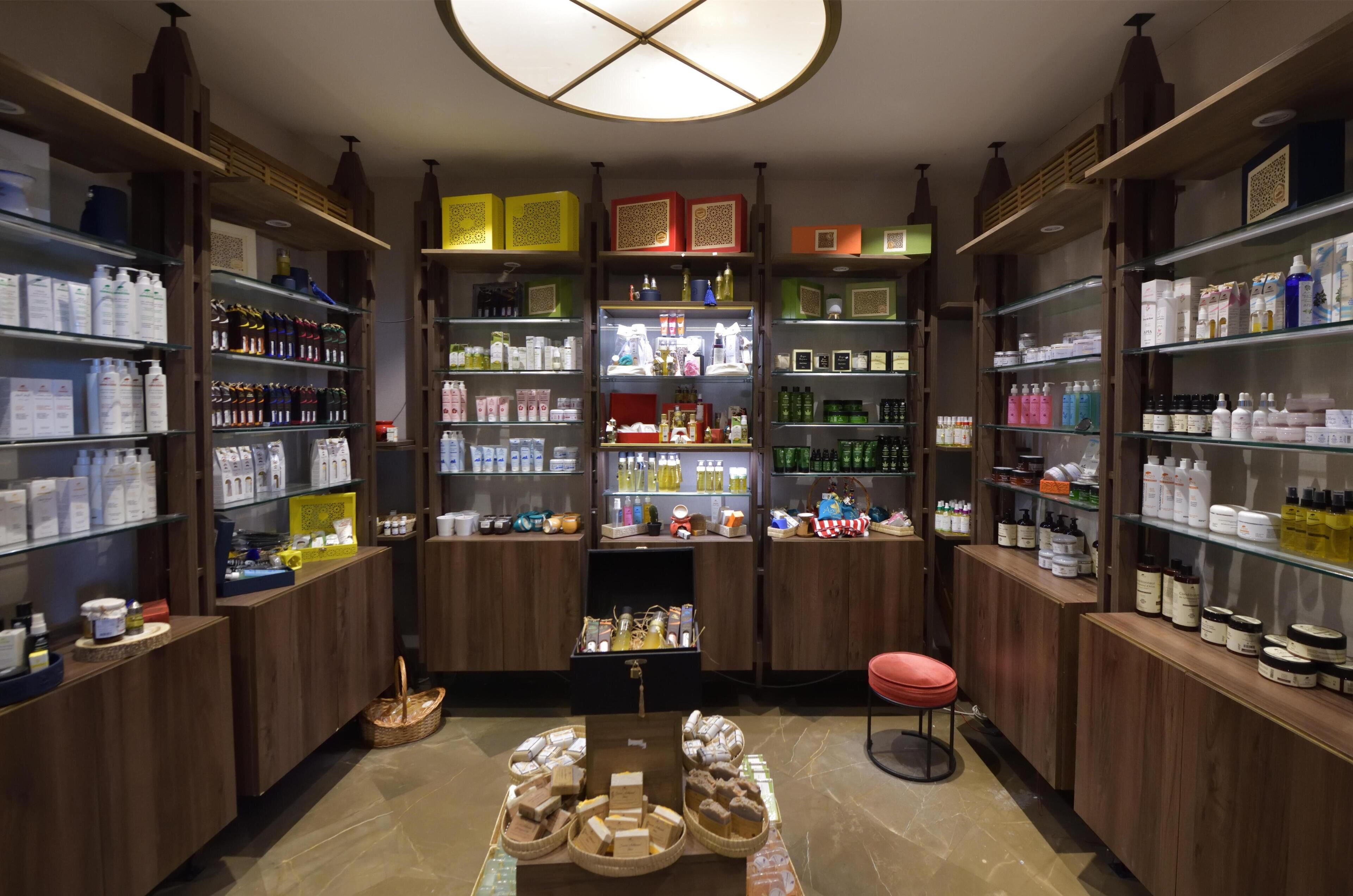 A well-organized store with shelves stocked with various products, a central display table, and a red stool.
