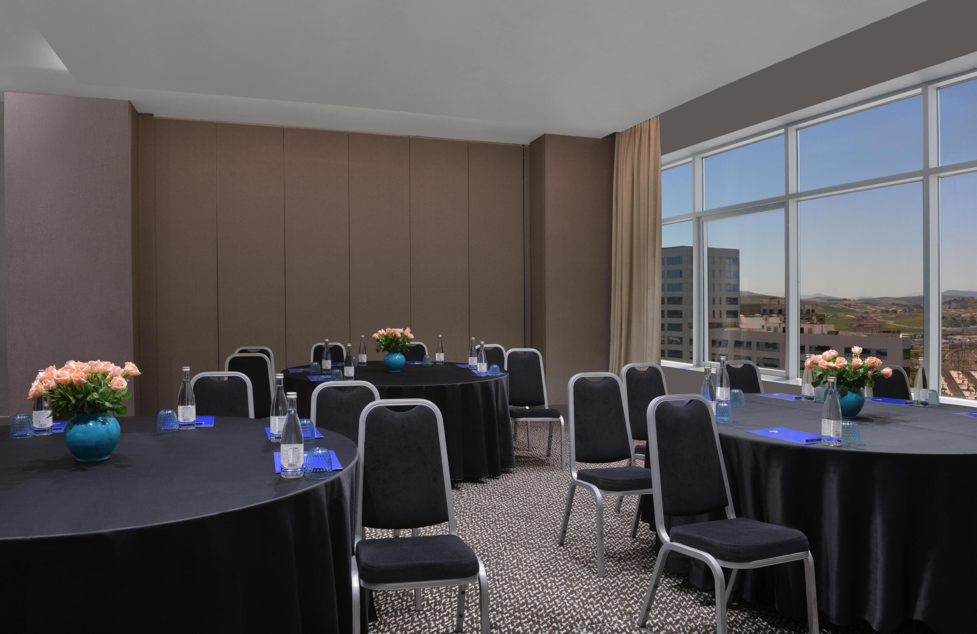 A conference room with tables, chairs, and a large window with a city view.