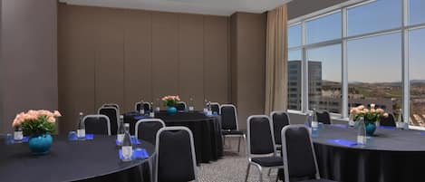 A conference room with tables, chairs, and a large window with a city view.