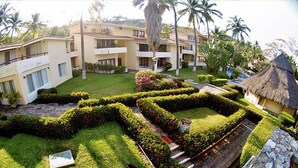 A resort with multiple-story buildings, manicured gardens, and a thatched-roof structure. - Villas del Palmar - Condo 704 (Manzanillo)