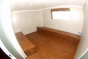 Une salle de bain avec un plancher en bois, des murs recouverts de carreaux blancs et une petite fenêtre.
