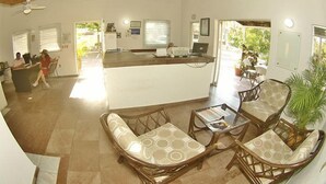 A spacious living area with a central island, wicker furniture, and a view of the outside. - Villas del Palmar - Condo 704 (Manzanillo)