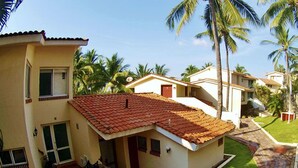 A residential building with a tiled roof, a patio area with outdoor furniture, and a stone wall. - Villas del Palmar - Condo 704 (Manzanillo)