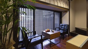 Una tradizionale stanza giapponese con pavimento in tatami, un tavolino con un set da tè, poltrone in pelle nera e un'ampia finestra con persiane verticali.