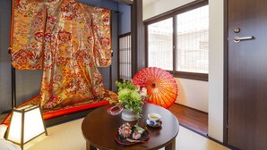 Una tradizionale stanza giapponese con pavimento in tatami, paravento shoji, tenda a righe rosse e bianche, un tavolo con un set da tè e un ombrello arancione.