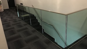 Una escalera moderna con barandillas de cristal y suelo alfombrado.