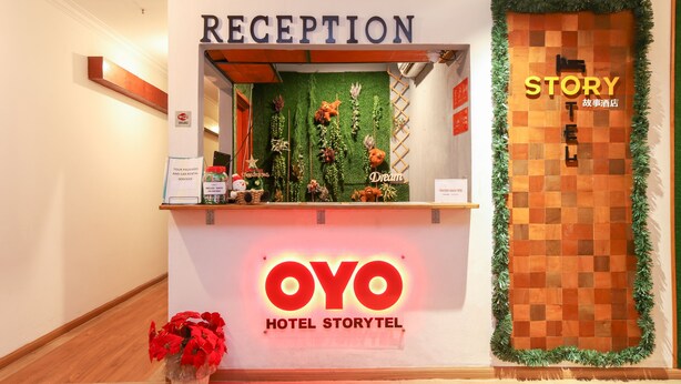 A hotel reception area with a 'RECEPTION' sign above a counter decorated with greenery and a 'Dream' sign. A 'STORYTEL' sign is visible on the wall, and a 'STORY' sign is on the door. - Hotel O Storytel (Kota Kinabalu)