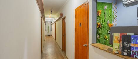 Un pasillo con puertas de madera, una pared verde con plantas y libros en una estantería.
