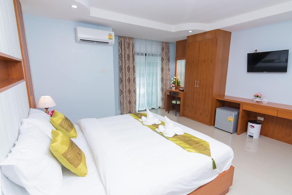 Una habitación de hotel con una cama bien hecha, un escritorio con una computadora, un televisor y un equipo de aire acondicionado.