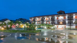 A multi-story hotel with a central courtyard, palm trees, and a reflective water feature. - Samrong Garden Resort (Udon Thani)