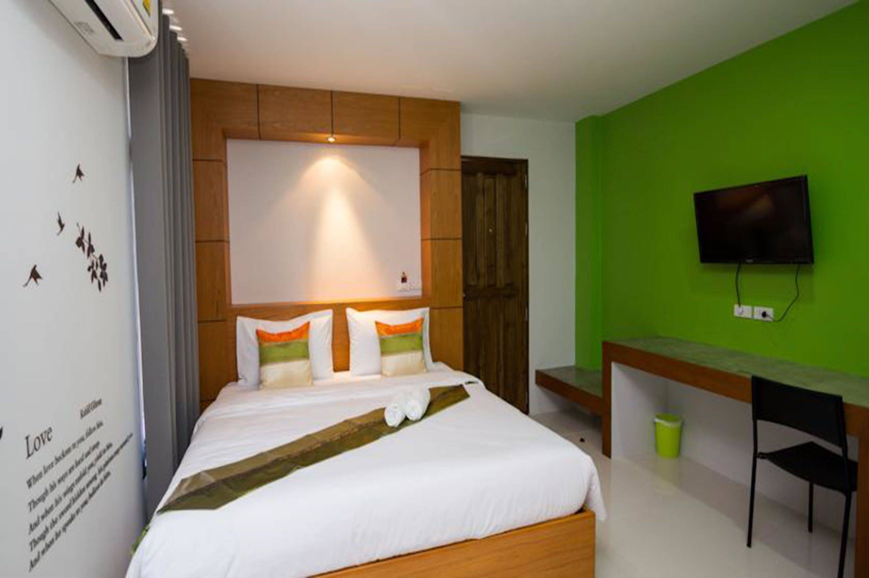 A hotel room with a bed, a desk, a television, and a green wall.