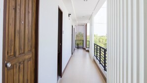 Un pasillo con una puerta de madera, un balcón con barandilla negra y vistas a la vegetación.