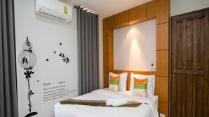 Habitación de hotel con cama, aire acondicionado de pared, armario de madera y una pared decorativa con una ilustración de un pájaro y texto.