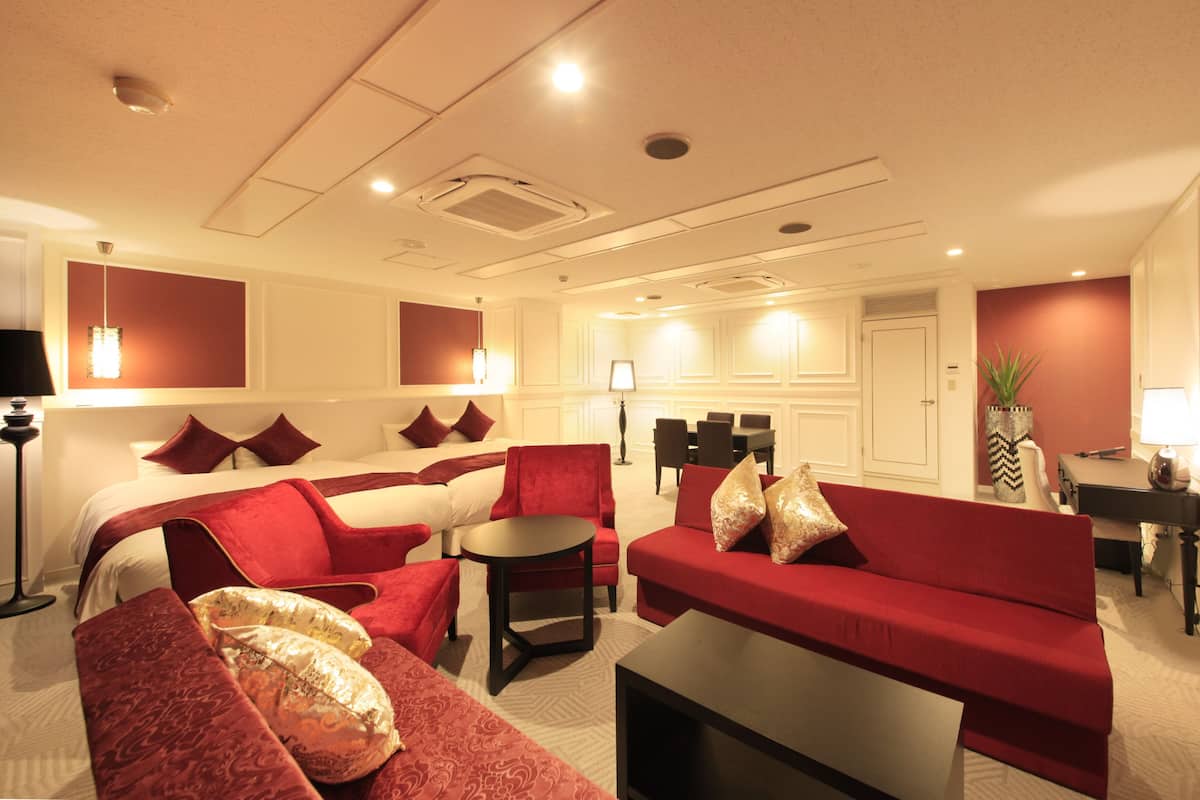 A hotel room with a red sofa, a round table, and a bed with white linens.