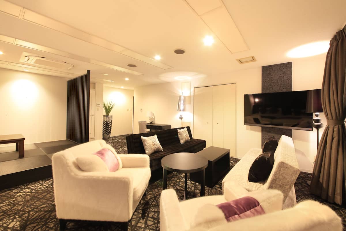 A hotel room with a sofa, two armchairs, a small table, a flat-screen TV, and a lamp.