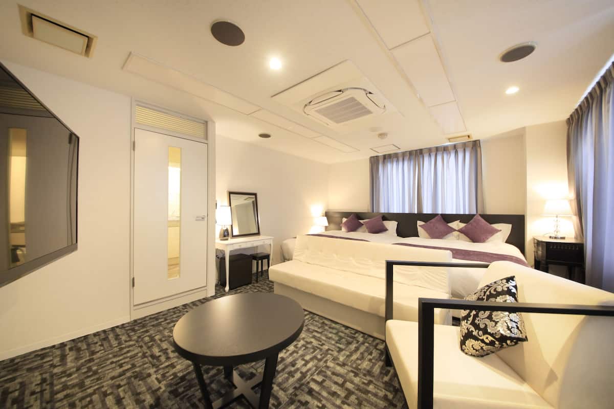 A hotel room with a bed, a desk, a chair, a small table, and a mirror.