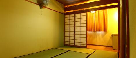 A traditional Japanese room with tatami flooring, a sliding door, and a ceiling fan.