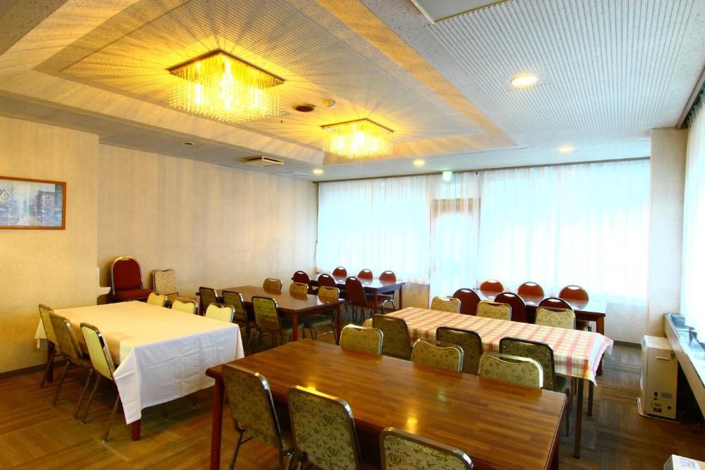 A conference room with multiple tables and chairs, a bed, and a large window with curtains.
