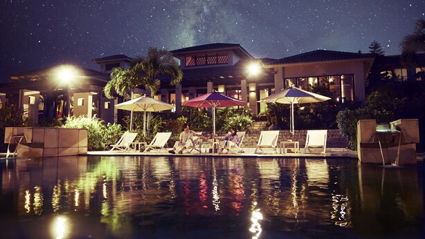 A pool area with lounge chairs and umbrellas, a building with a sign, and a starry night sky. - Hoshino Resorts RISONARE Kohamajima (Taketomi)