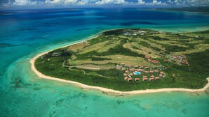 An aerial view of a tropical island with a beach, a resort area with red-roofed buildings, and clear turquoise waters. - Hoshino Resorts RISONARE Kohamajima (Taketomi)