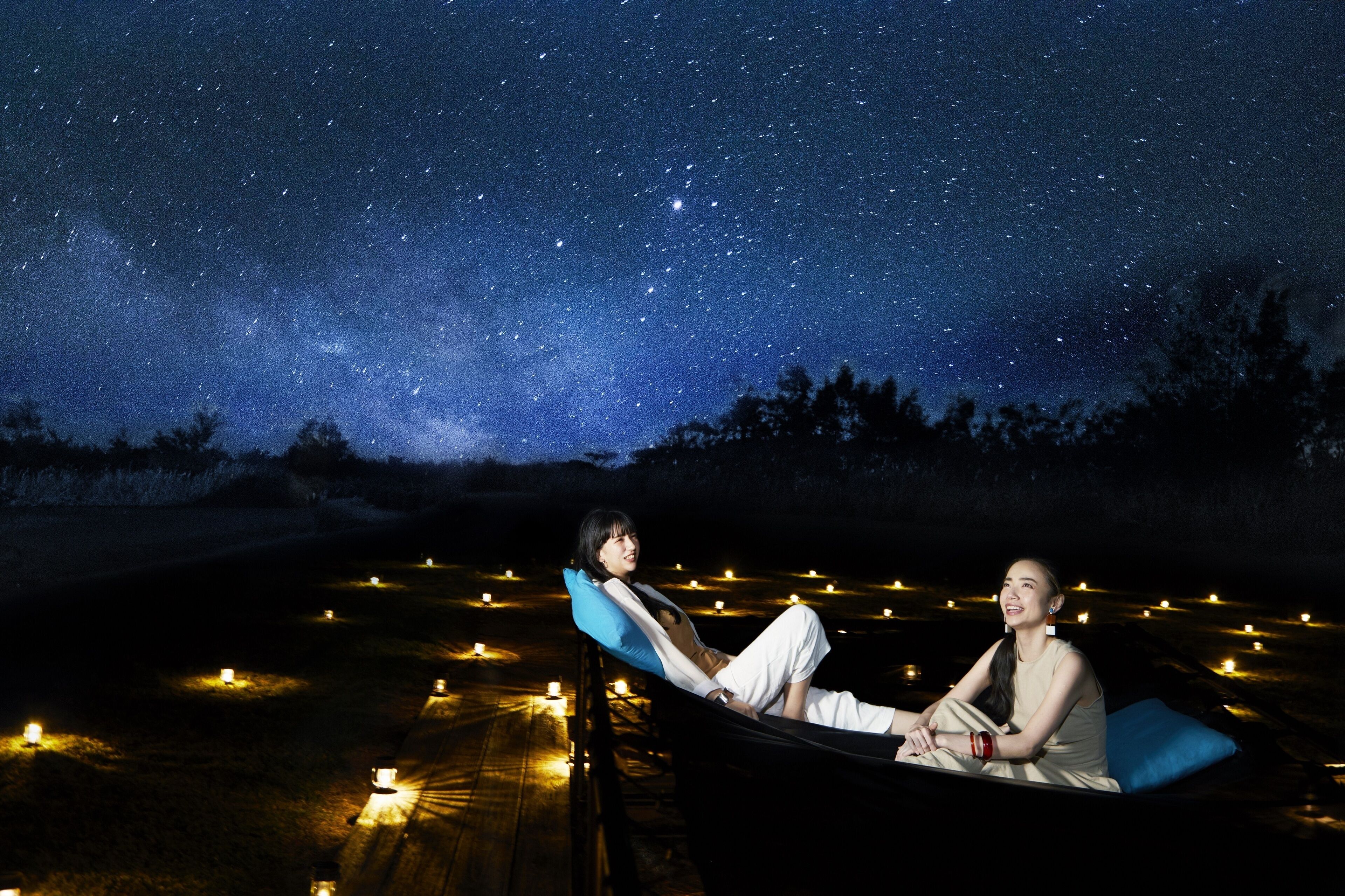 Two people reclining on a boat in a starry night sky.