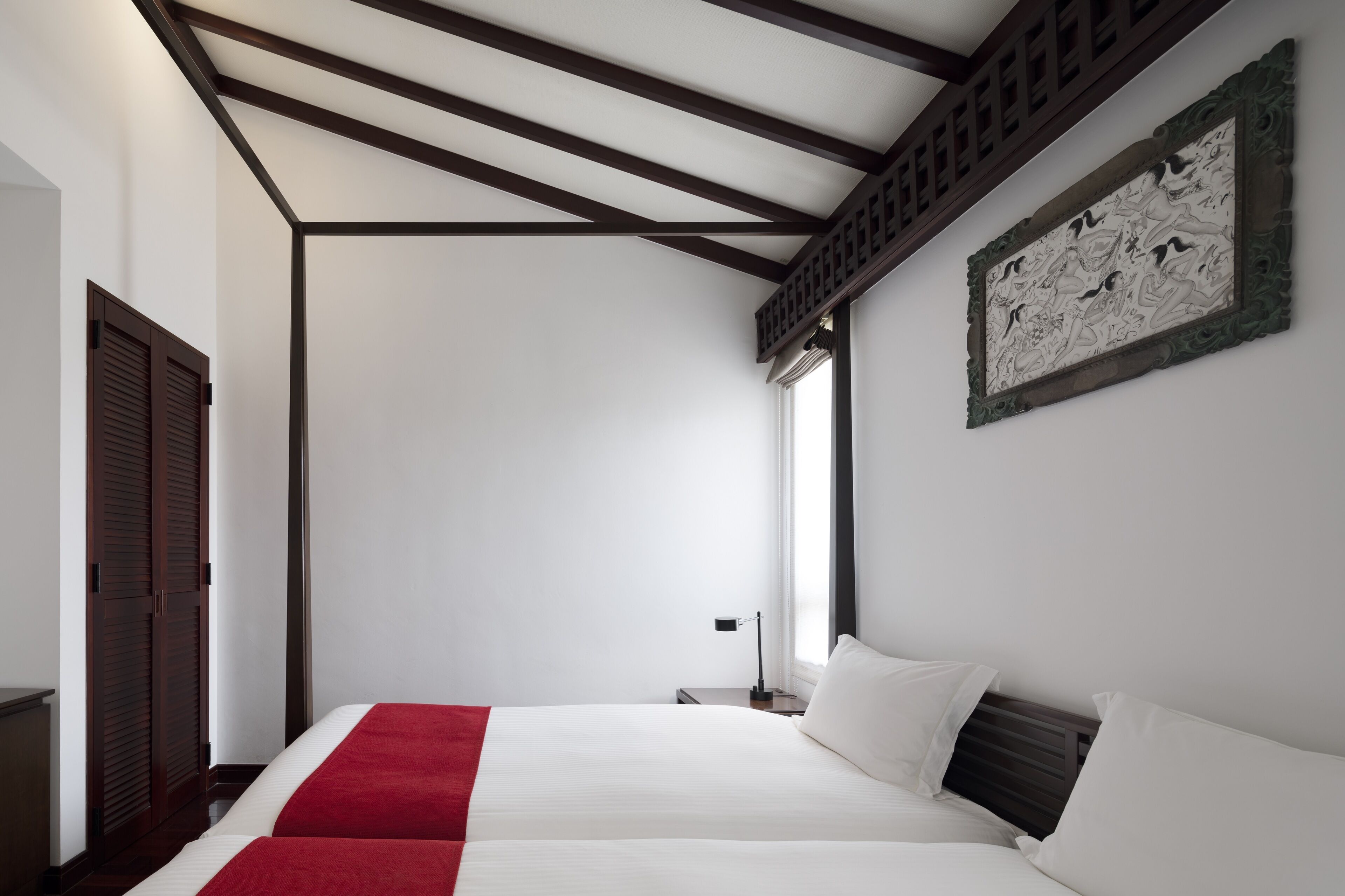 Une chambre d’hôtel avec un grand lit, un plafond en bois, une œuvre d’art accrochée au mur et une fenêtre avec des rideaux.
