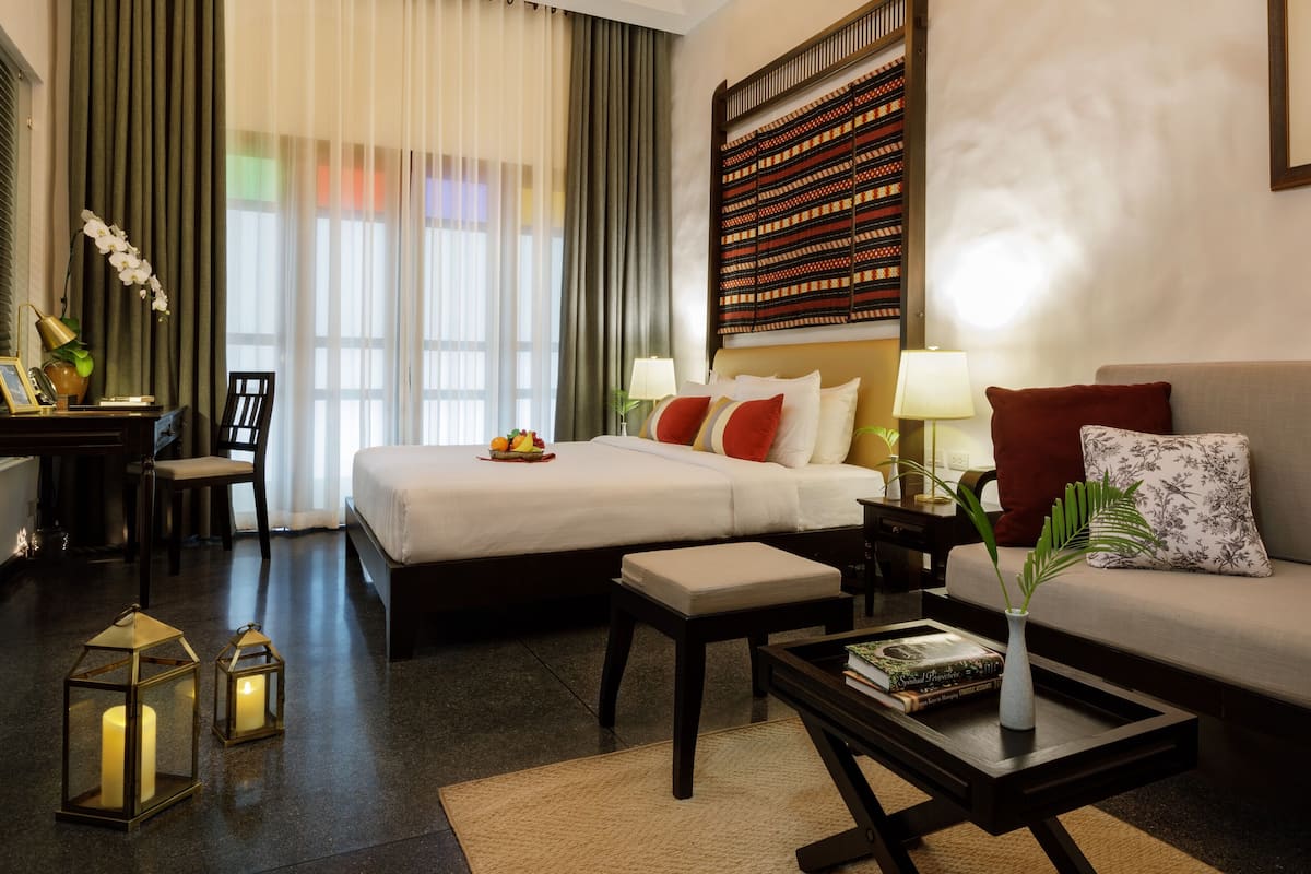 A hotel room with a bed, sofa, desk, and lamp.