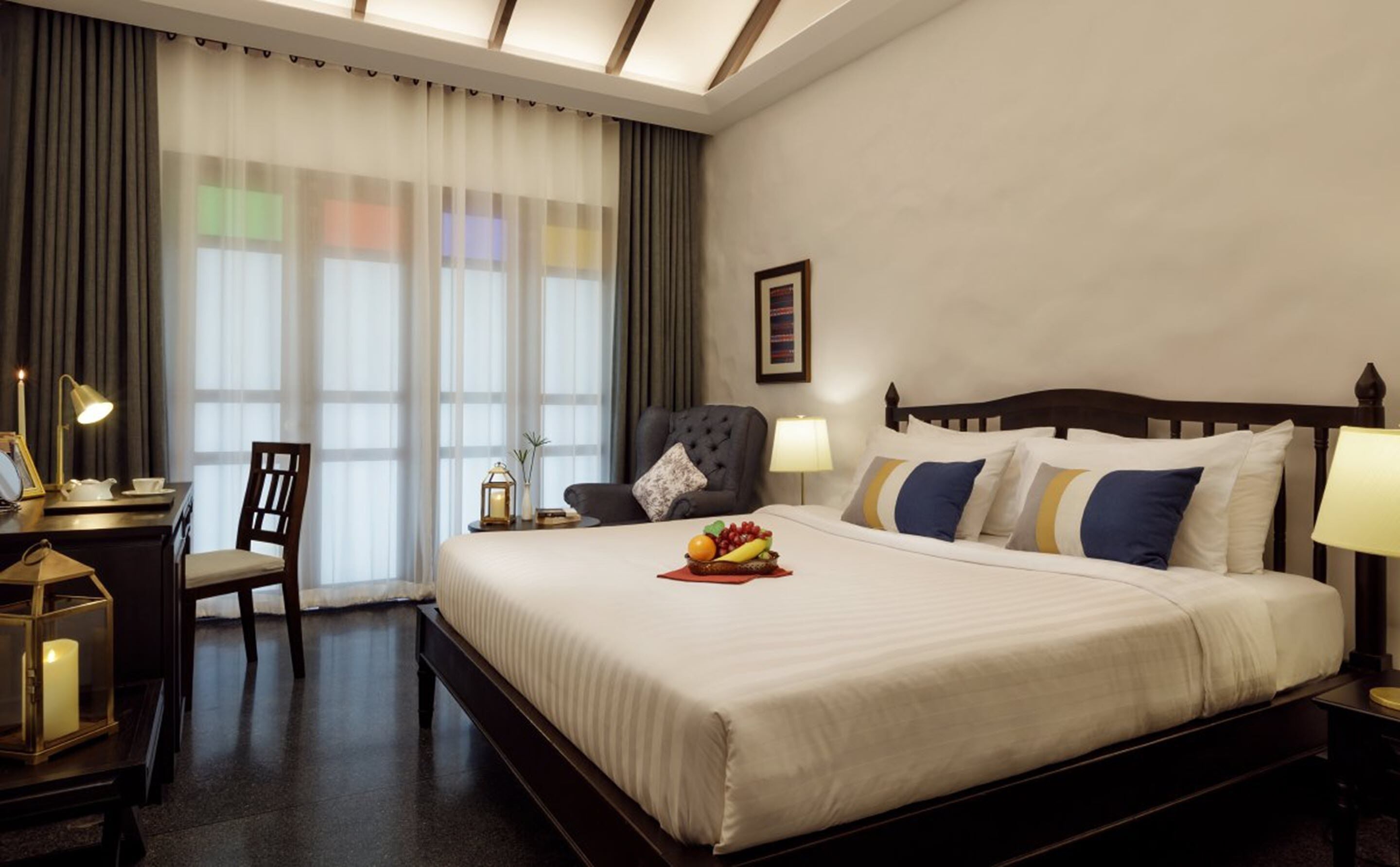 A hotel room with a large bed, a desk with a lamp, a chair, and a nightstand with a lamp.