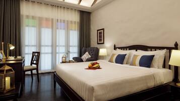 A hotel room with a large bed, a desk with a lamp, a chair, and a nightstand with a lamp.