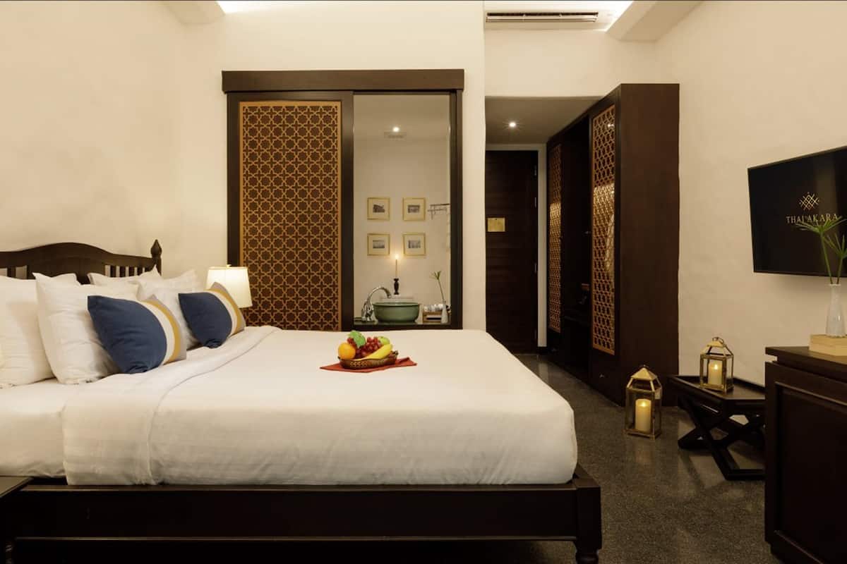 A hotel room with a bed, bedside lamps, a nightstand, a TV, and a bathroom visible through a sliding door.
