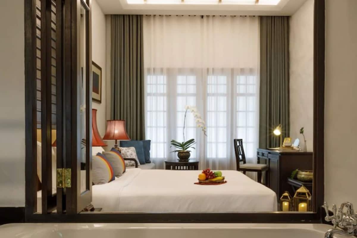 A modern hotel room with a large bed, a bathtub, and a mirror reflecting the room.